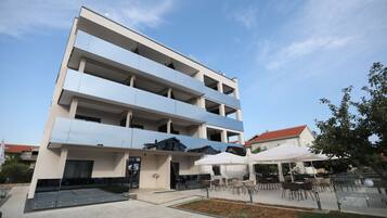 A multi-story hotel with a flat facade, outdoor seating area, and a clear sky.