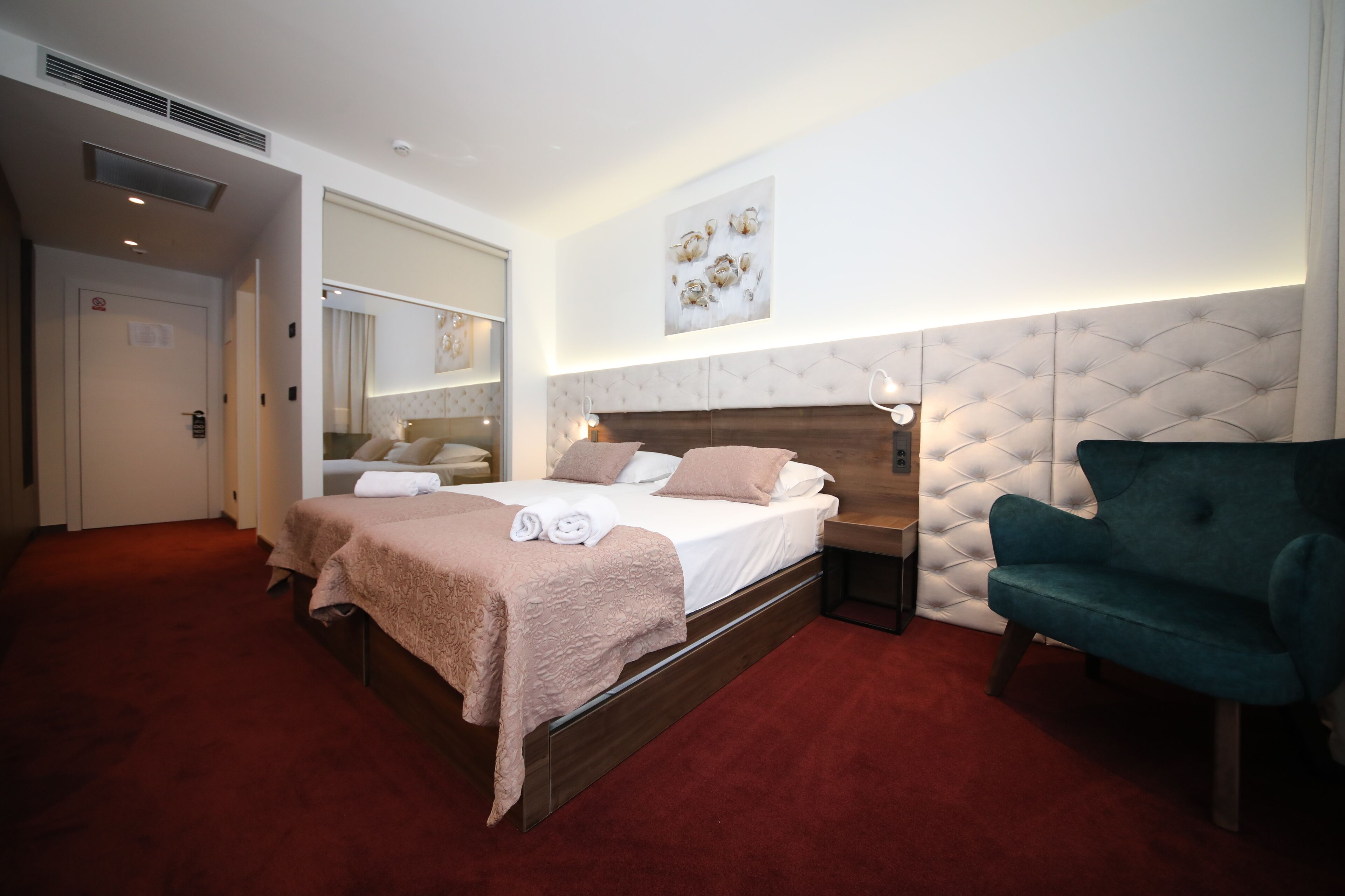 A hotel room with a large bed, a bedside table, a green armchair, and a wall-mounted artwork.