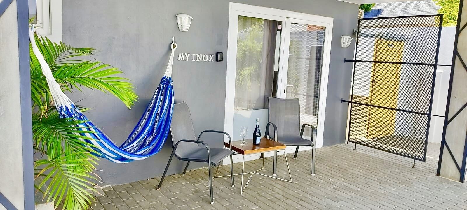 A patio with a hammock, two chairs, a table with a bottle, and a gate.