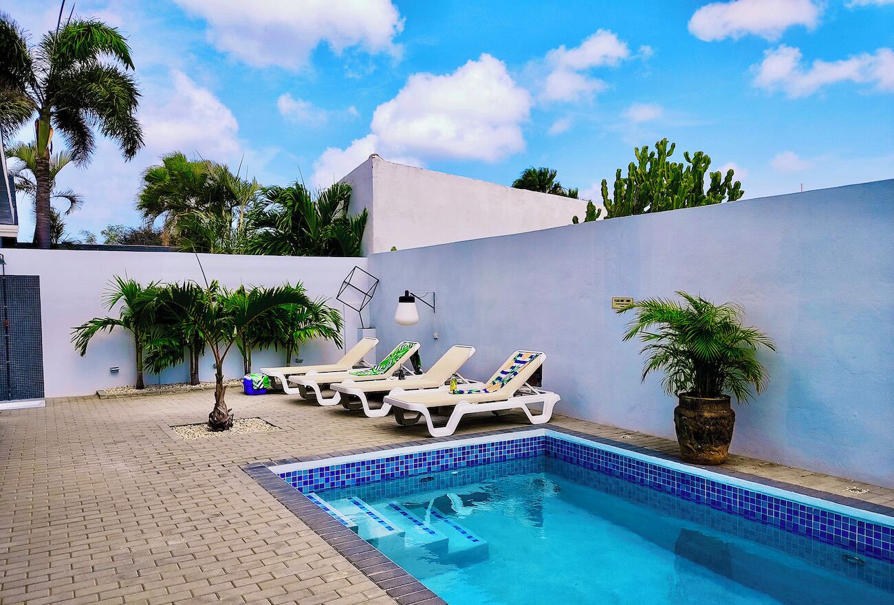 A swimming pool with lounge chairs, palm trees, and a tiled deck.