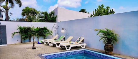 A swimming pool with lounge chairs, palm trees, and a tiled deck.