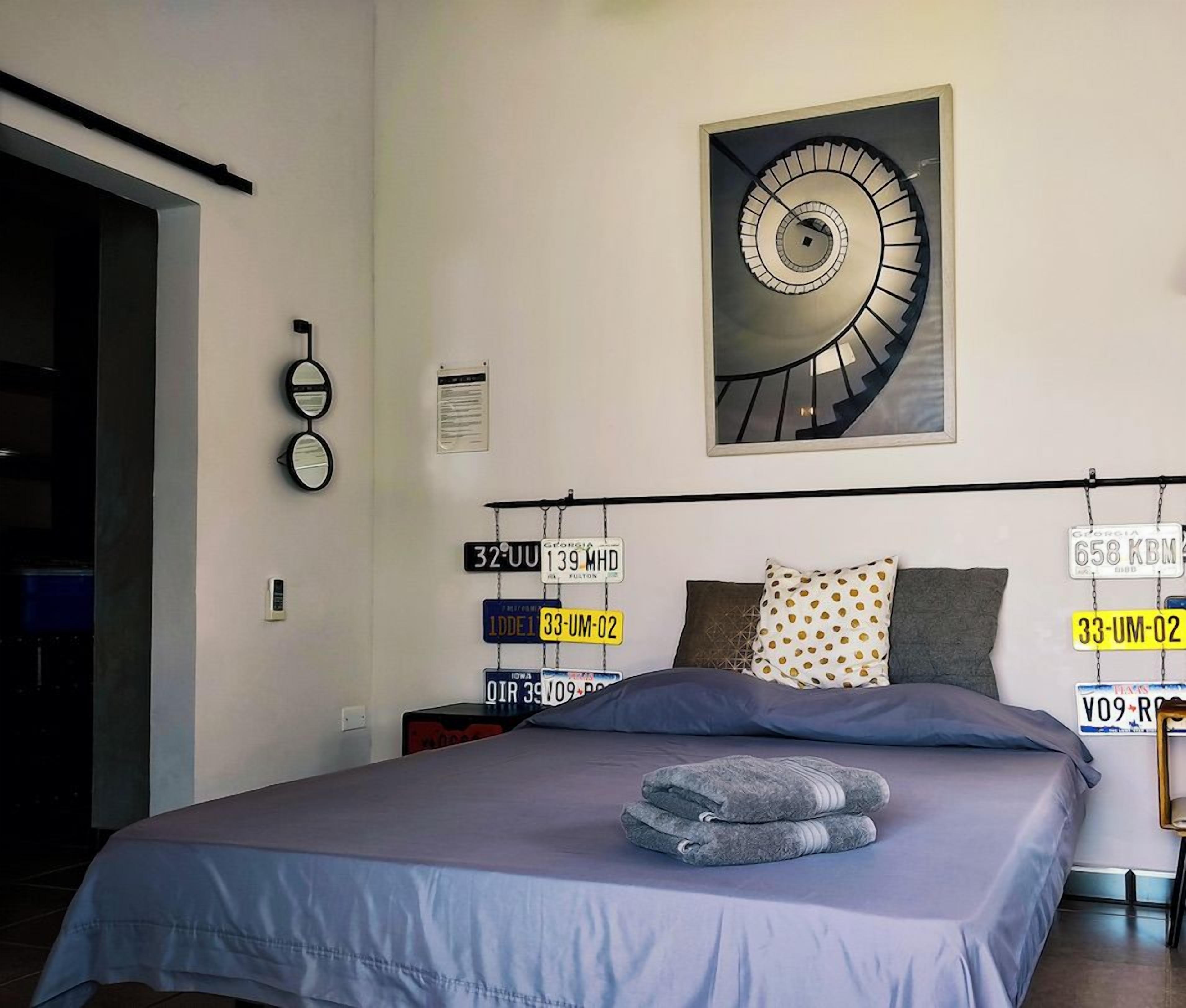 Ein Schlafzimmer mit einem Bett, Kissen, einer Wandleuchte und einem Bild von einer Wendeltreppe.