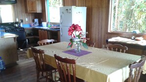 A wooden dining table with chairs, a vase with flowers, and a kitchen area with wooden cabinets and appliances. - Naturalist's Cloud Forest Retreat (Monteverde)