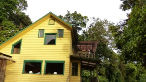 A yellow house with a wooden porch and a small balcony. - Naturalist's Cloud Forest Retreat (Monteverde)
