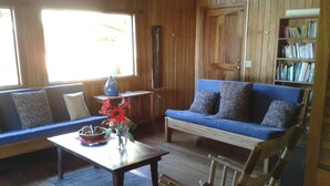 A wooden interior with a blue sofa, a wooden chair, a coffee table with a vase of flowers, and a bookshelf. - Naturalist's Cloud Forest Retreat (Monteverde)