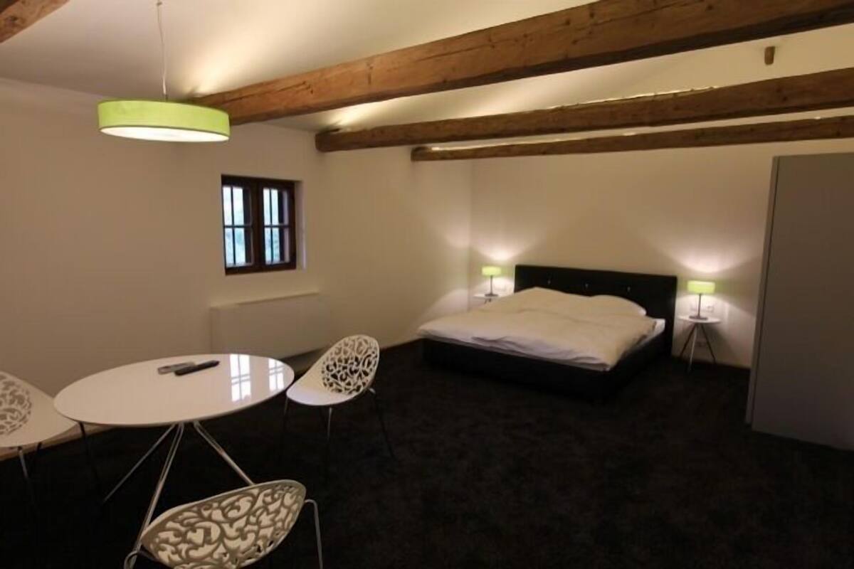 A small, cozy room with a bed, two chairs, a table, and a window.