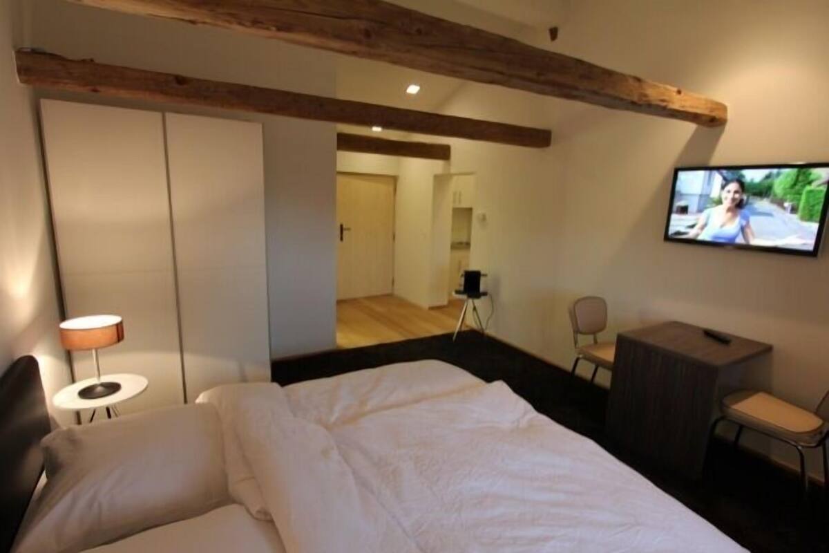 A hotel room with a bed, a TV mounted on the wall, a desk, and a chair.