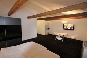 Habitación de hotel con cama, televisor, una pequeña mesa con sillas y vigas de madera a la vista.