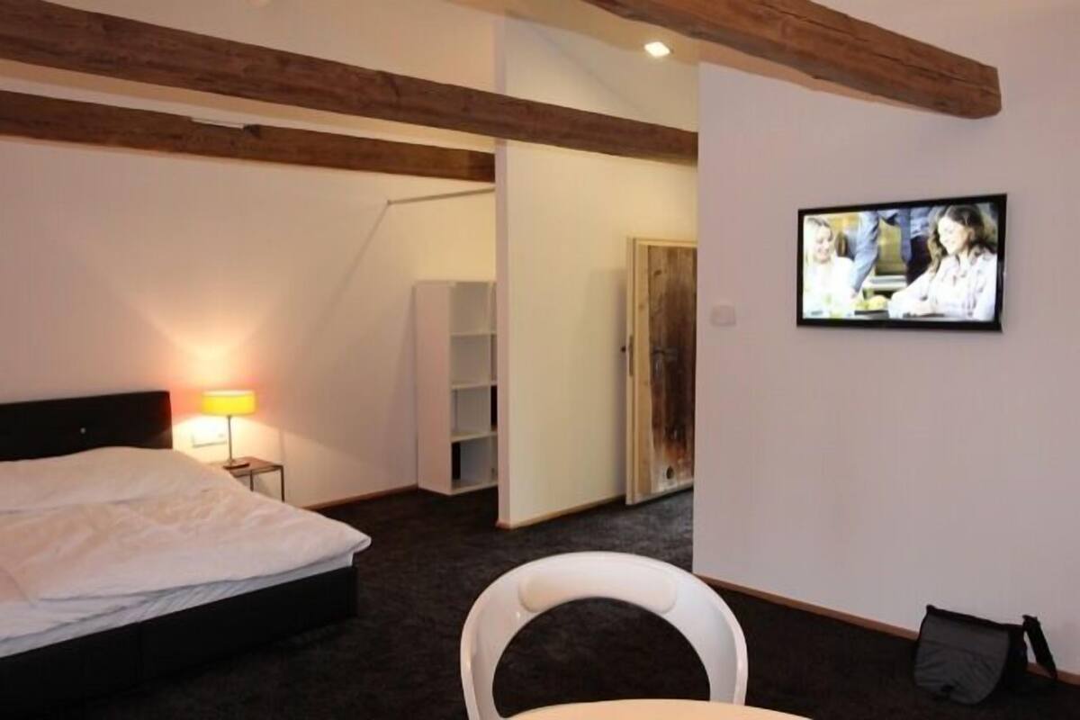 A hotel room with a bed, a TV mounted on the wall, a chair, and a small table.