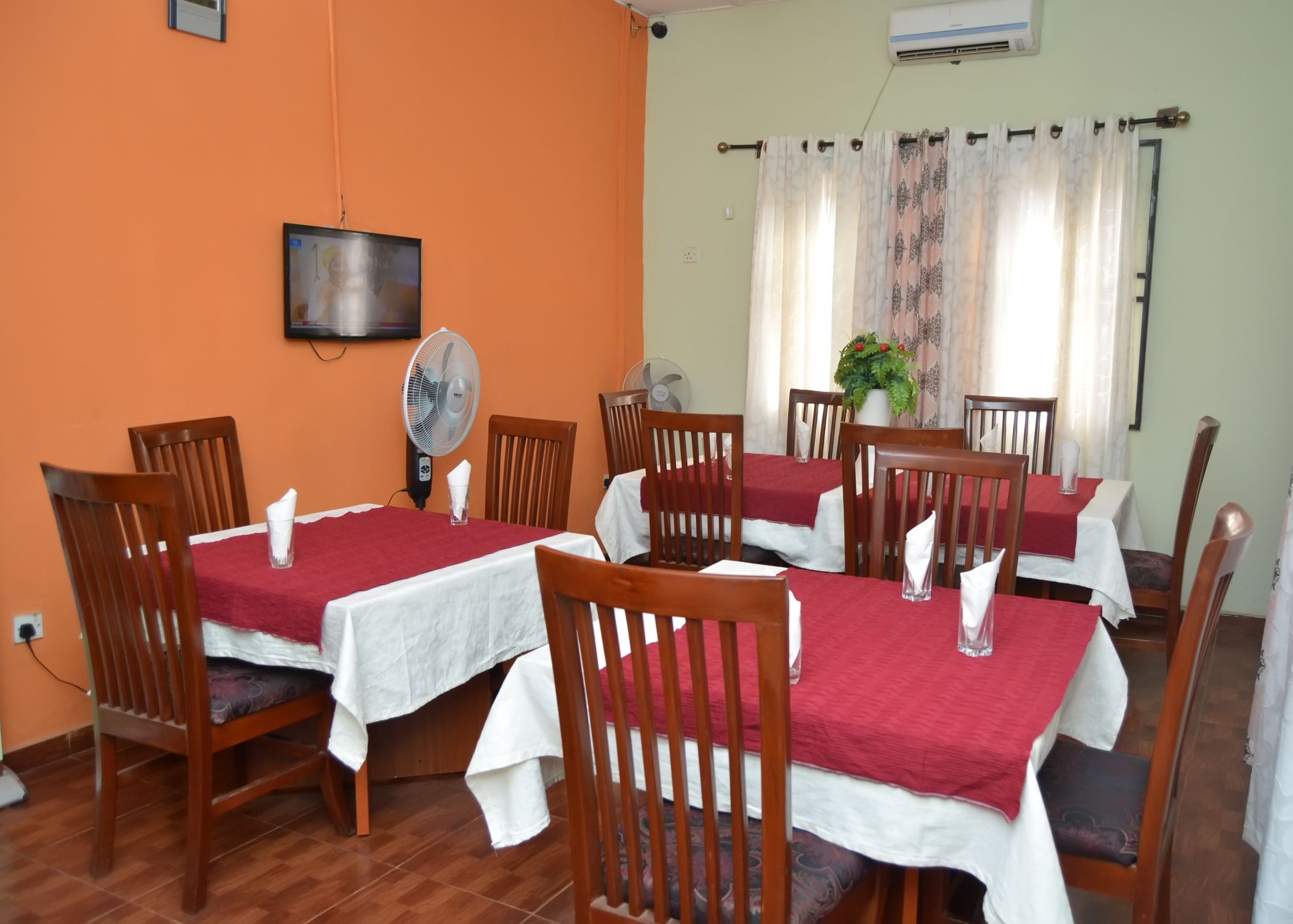 A dining area with wooden chairs and tables, a wall-mounted TV, and a fan.