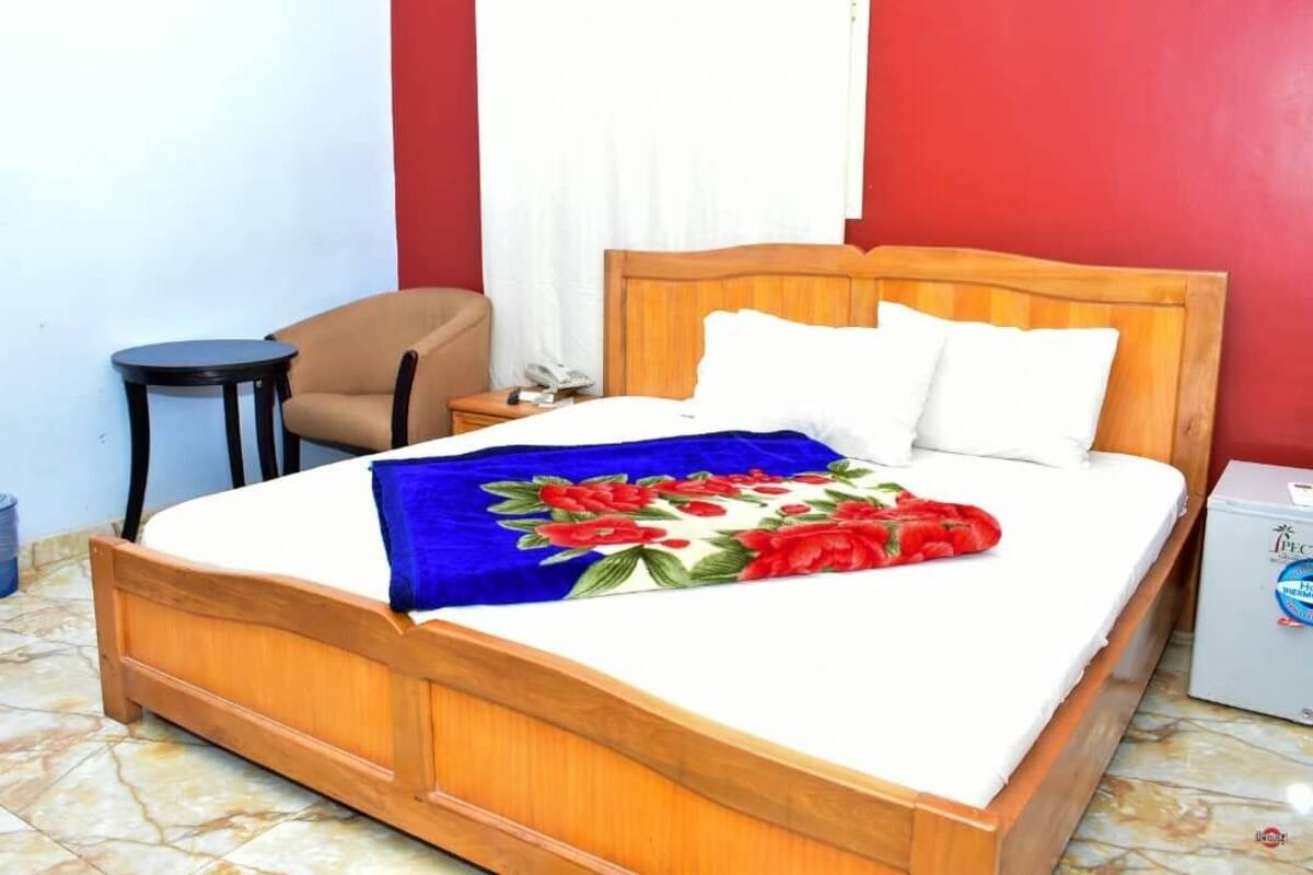 A bed with a floral bedspread, a wooden headboard, a bedside table, a chair, and a small white cabinet.