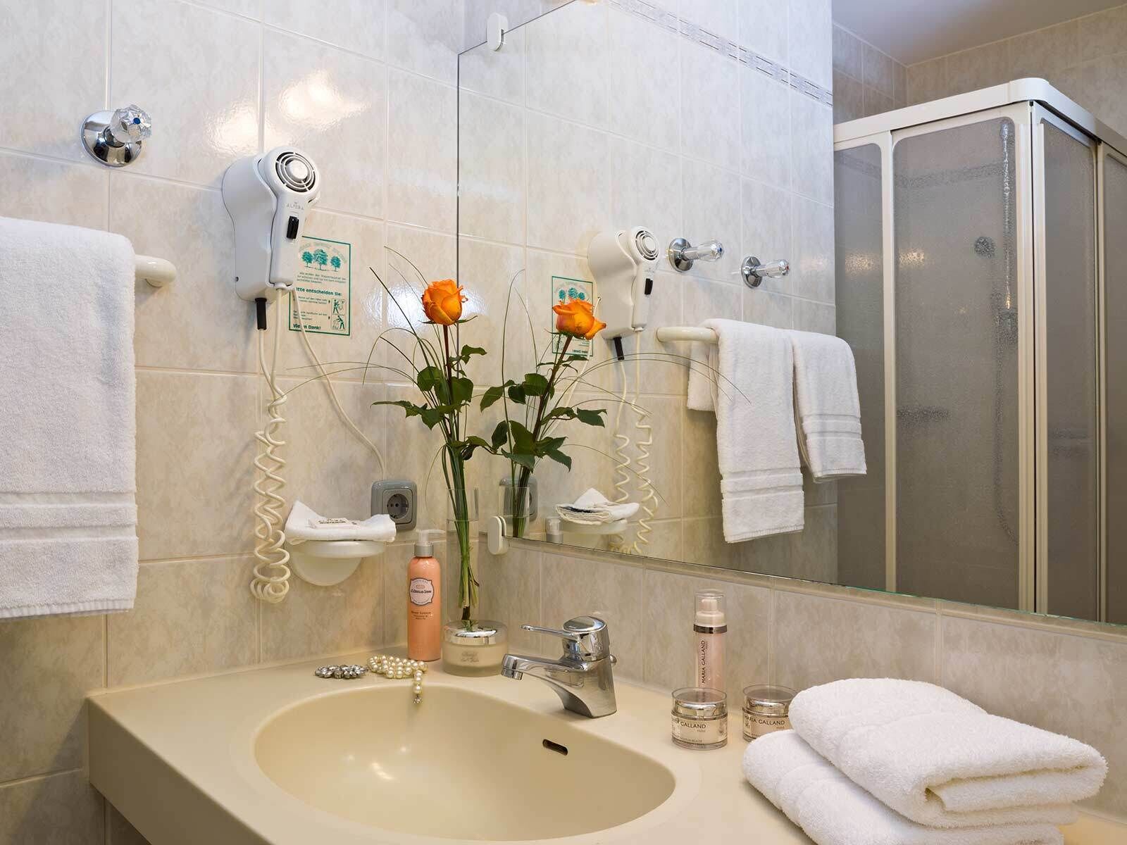Un baño con lavamanos, espejo y dos secadores de pelo fijos en la pared.