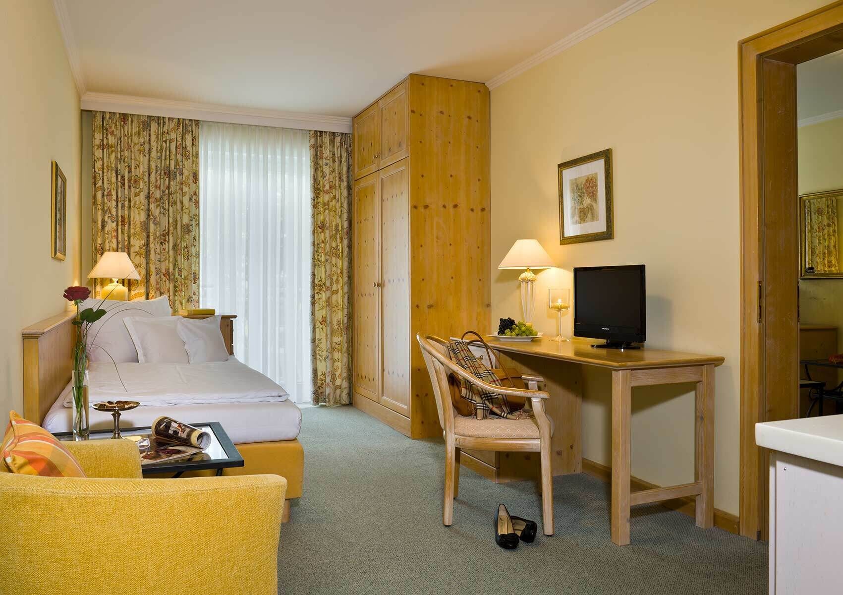 Habitación de hotel con cama, escritorio con computadora, silla, una mesita con lámpara y televisor.