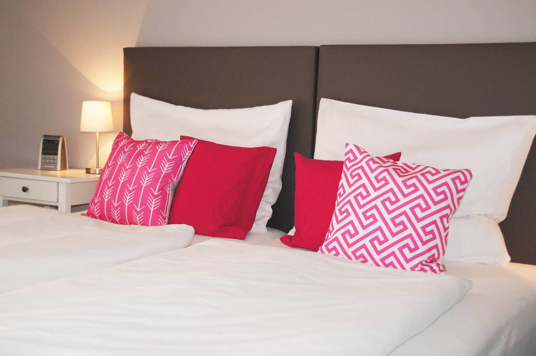 Una cama con ropa de cama blanca y dos almohadas, una con diseño de hojas y otra con diseño de zigzag.