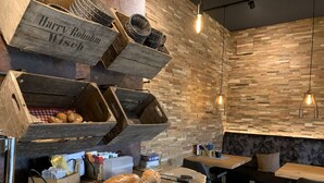 A rustic bakery setup with wooden shelves displaying bread and baskets, a wooden table with loaves of bread, and a seating area with a bench and table. - Hotel Dein Franz (Bad Fuessing)