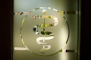 A glass door with a dollar sign etched into it, reflecting a street scene with a car and greenery. - Hotel Dein Franz (Bad Fuessing)