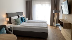 A modern hotel room with a large bed, bedside tables, a desk, a chair, a TV, and a large window with curtains. - Hotel Dein Franz (Bad Fuessing)