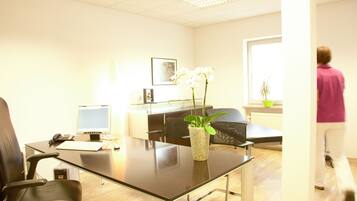 A modern office with a glass table, black office chairs, a computer, and a vase with white flowers.