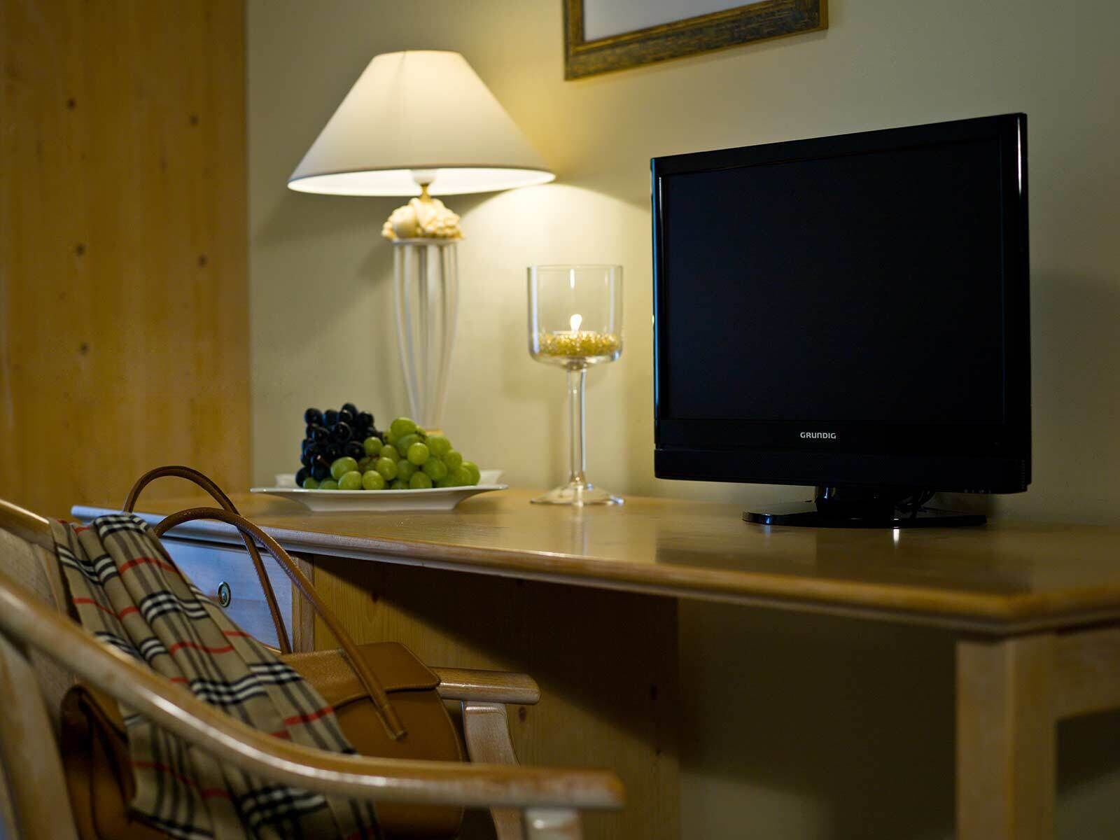 A hotel room with a wooden desk, a television, a lamp, and a bowl of grapes.