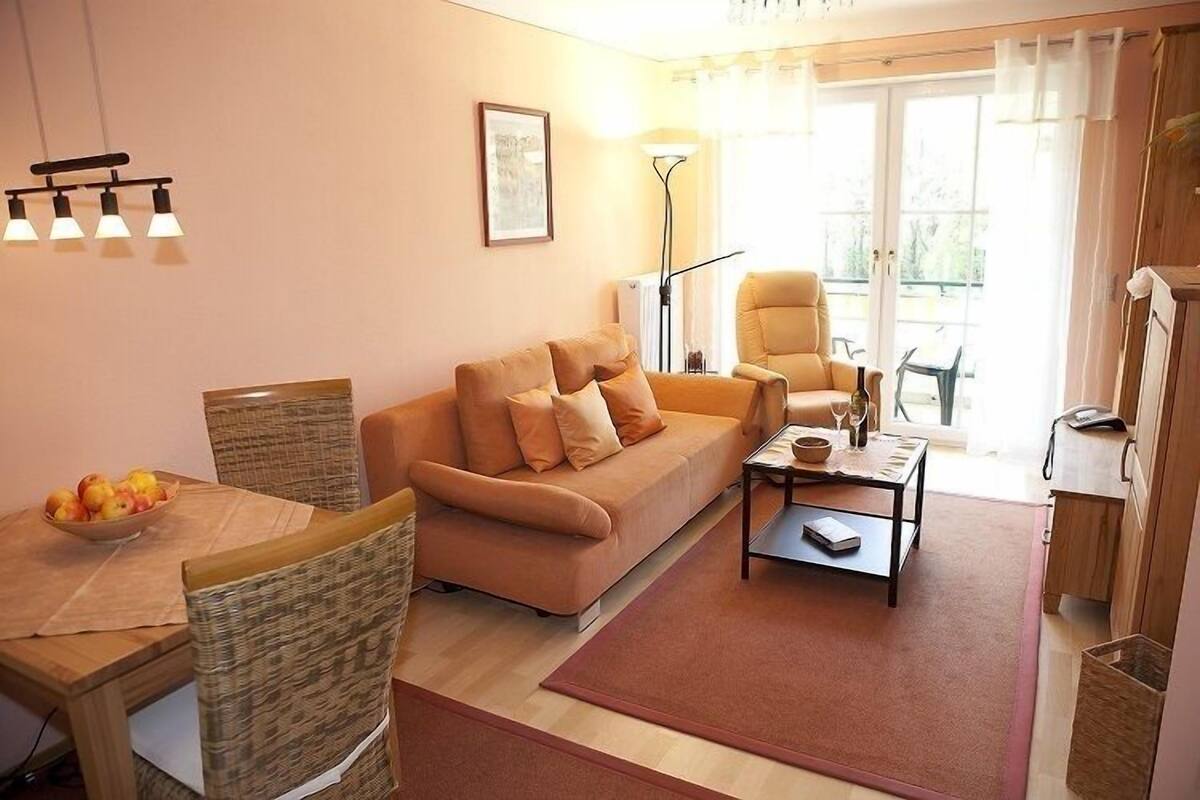 A cozy living room with a sofa, chairs, a dining table with fruit, a coffee table, and a lamp.