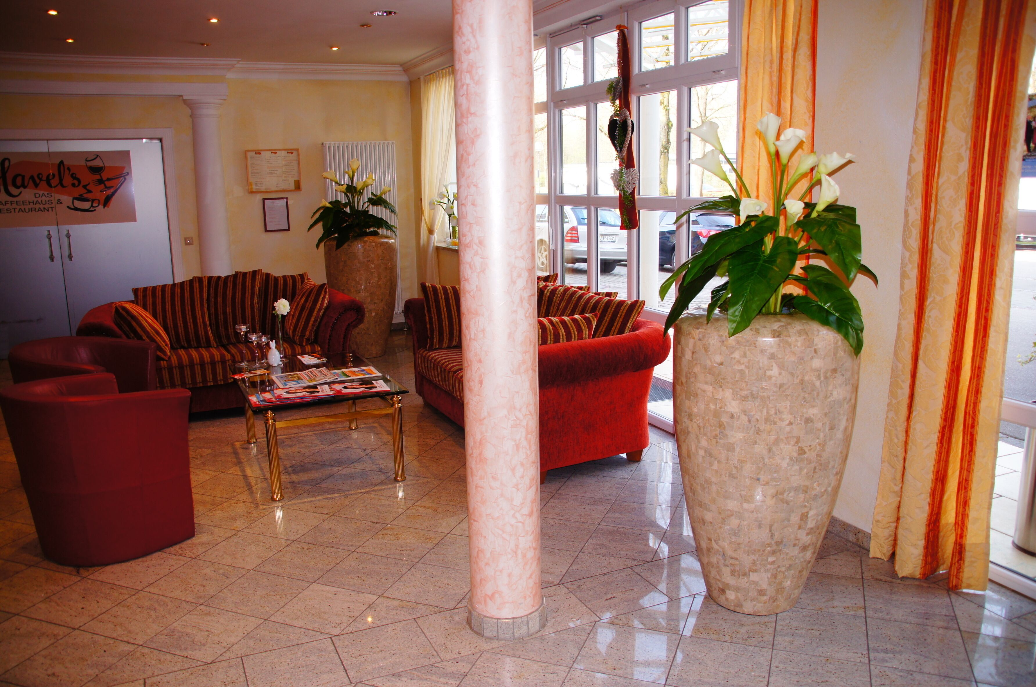 Een hotel lobby met een rode zithoek, een bijzettafeltje en een grote potplant.