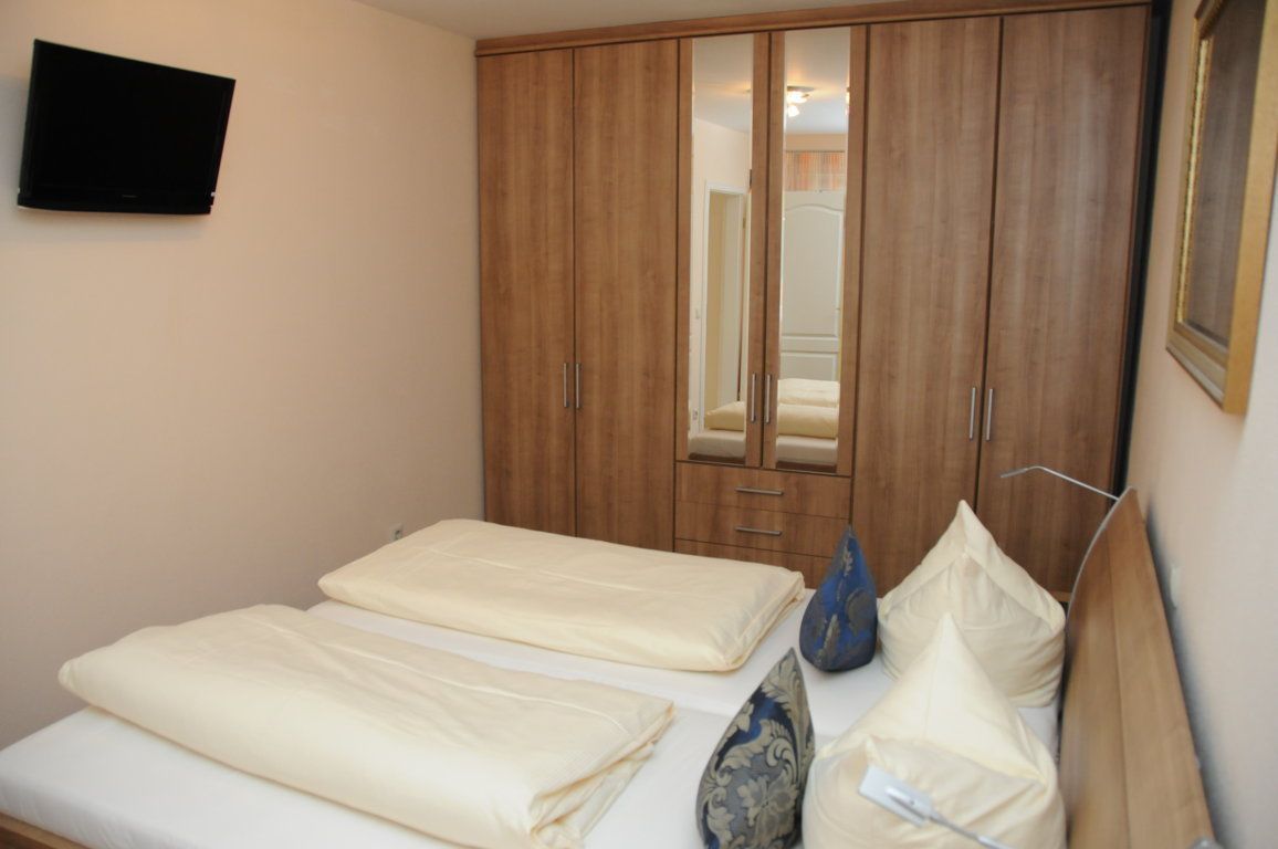 A bedroom with two beds, a wardrobe, a television, and a mirror.
