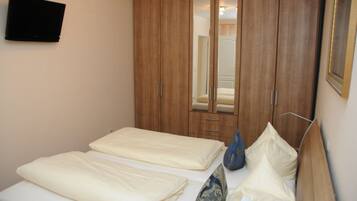 A bedroom with two beds, a wardrobe, a television, and a mirror.