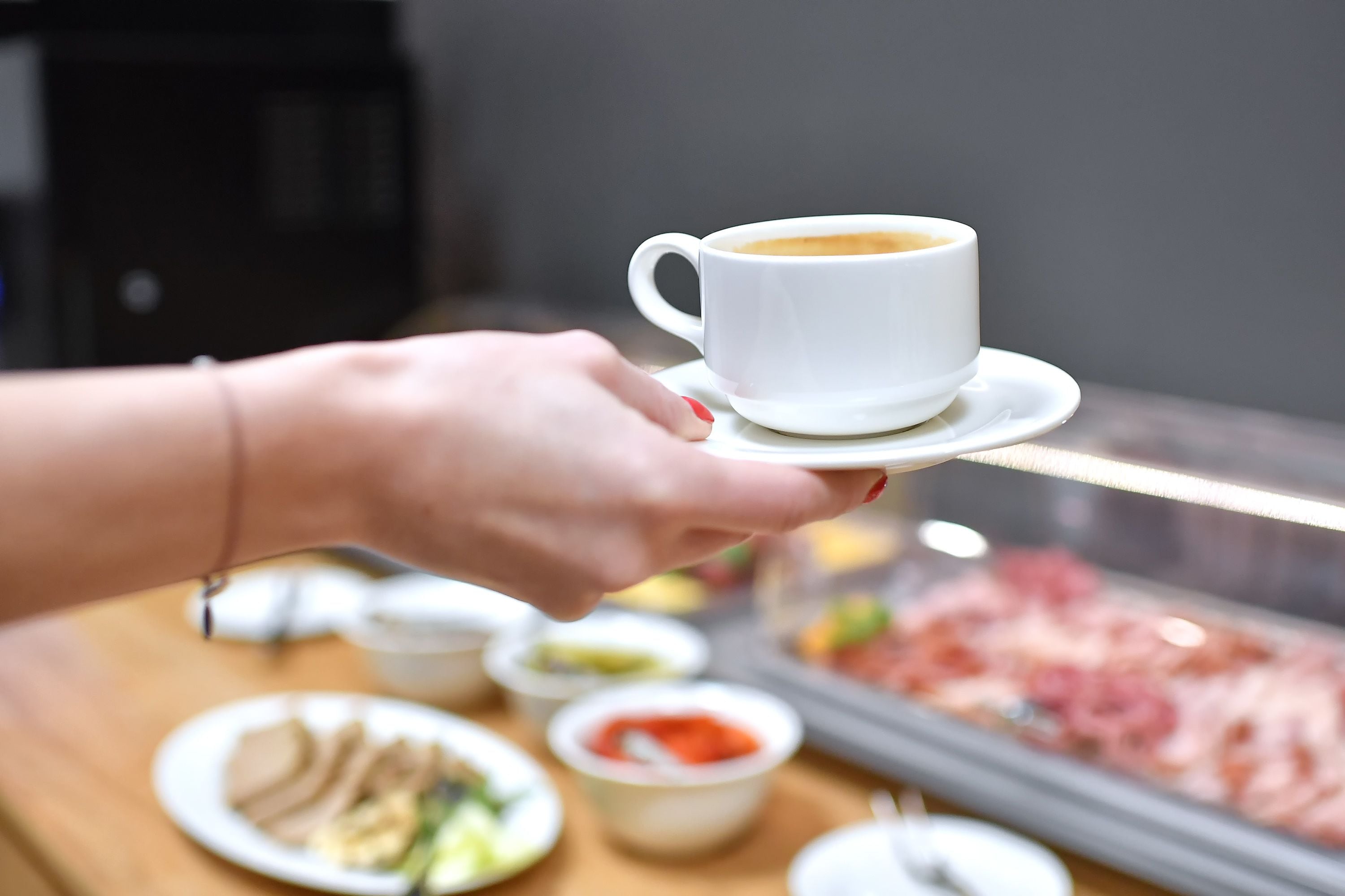 A hand holding a white cup of coffee on a saucer.
