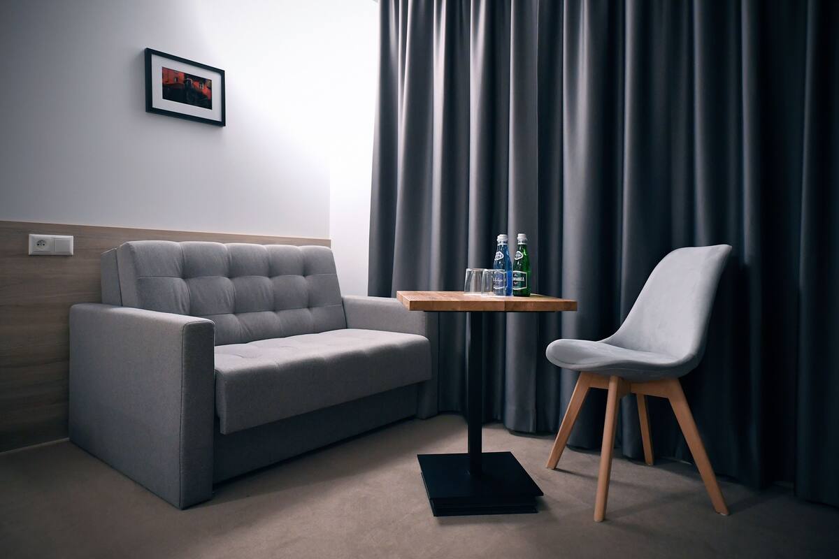 Una habitación de hotel moderna con un sofá gris, una pequeña mesa de madera con botellas y un sillón gris.