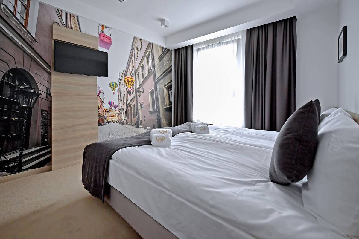 Una habitación de hotel moderna con una cama grande, un televisor de pantalla plana y un mural de una escena callejera en la pared.