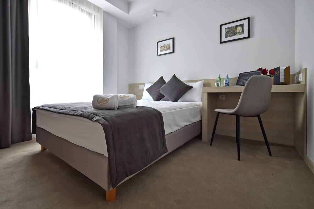 Habitación de hotel con cama, escritorio, silla y ventana con cortinas.