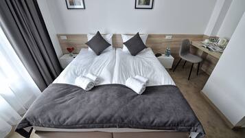 A hotel room with a double bed, two pillows, a desk with a chair, and a small table with a vase of flowers.