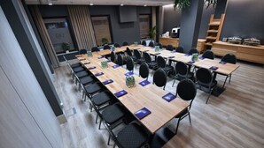 Un salón de conferencias con mesas largas, sillas y portátiles.