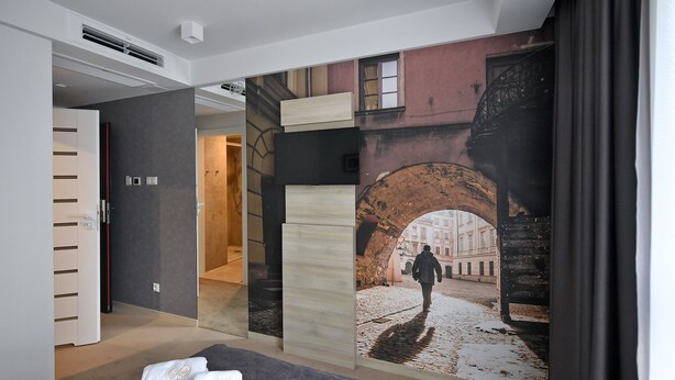 Una habitación de hotel con una cama, un gran mural de una escena callejera y una puerta que conduce a otra habitación.