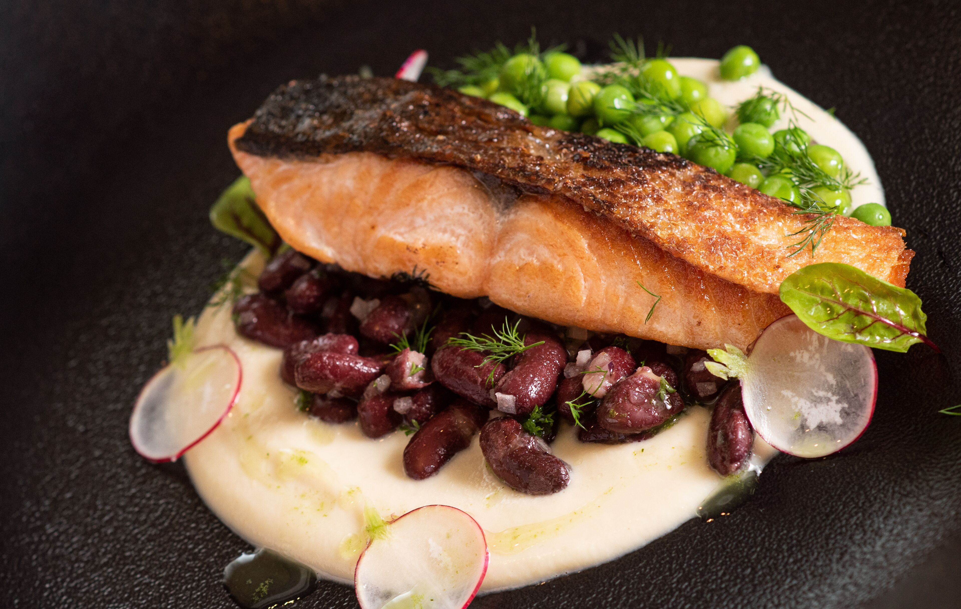 Een bord met zalm, erwten, bonen en radijsjes.