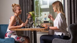 Dos personas sentadas en una mesa de madera, con un jarrón de flores, una copa de vino y un plato de comida.
