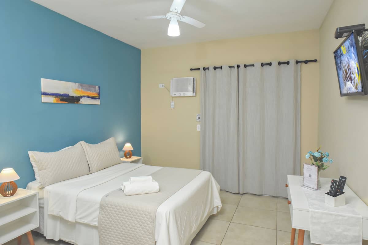 Une chambre d’hôtel avec un lit, des tables de chevet, un ventilateur de plafond, une télévision et une fenêtre avec des rideaux.