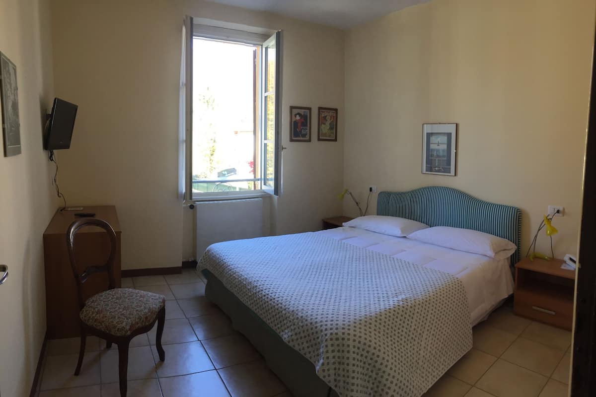 A bedroom with a bed, a chair, a desk, and a window.