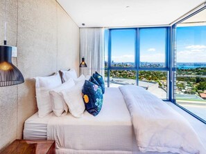 Ein modernes Schlafzimmer mit einem großen Bett, Blick auf die Stadt und einer Stadtansicht durch große Fenster.