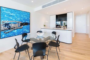 Una cucina moderna con mobili bianchi, un'isola in vetro e sedie nere attorno a un tavolo in vetro.