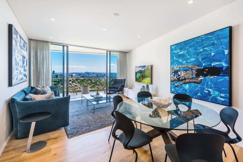 A modern living room with a glass table, black chairs, a blue sofa, and a large abstract painting.