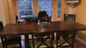 A dining area with a large wooden table and chairs, a television mounted on the wall, and a view of the outdoors through large windows. - Fun Seekers Getaway!!!! (Hot Springs)