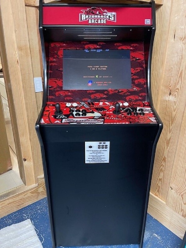 Een Razorbacks spelcomputer met een rood en zwart ontwerp, een joystick en een scherm dat informatie over het spel toont.