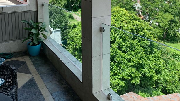 Ein Balkon mit Fliesenboden, einem Blumentopf und Blick auf eine Stadtlandschaft mit Gebäuden und Grünflächen.