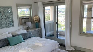 Ein Schlafzimmer mit einem großen Bett, einer Bank, einer Kommode und Blick auf die Stadt durch das Fenster.