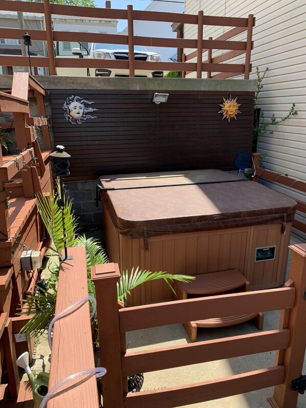 A hot tub with a wooden deck, surrounded by a wooden fence and plants.