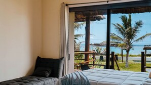 Una habitación con cama, un banco y vista al océano a través de un ventanal grande.
