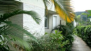 A pathway flanked by lush greenery and a white building with a curved roof. - BEAUTIFUL HOUSE CAMBURY Gated Community 5 Bedrooms 300mts from the Beach, Camburi, S.Sebastião (SÃO SEBASTIÃO)