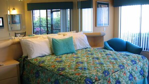 Ein Hotelzimmer mit einem großen Bett, einem Sessel, einem Nachttisch und einem Fenster mit Blick auf Grünflächen.