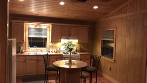 Una cocina con armarios de madera, una mesa redonda con sillas, una estufa y una ventana con persianas.